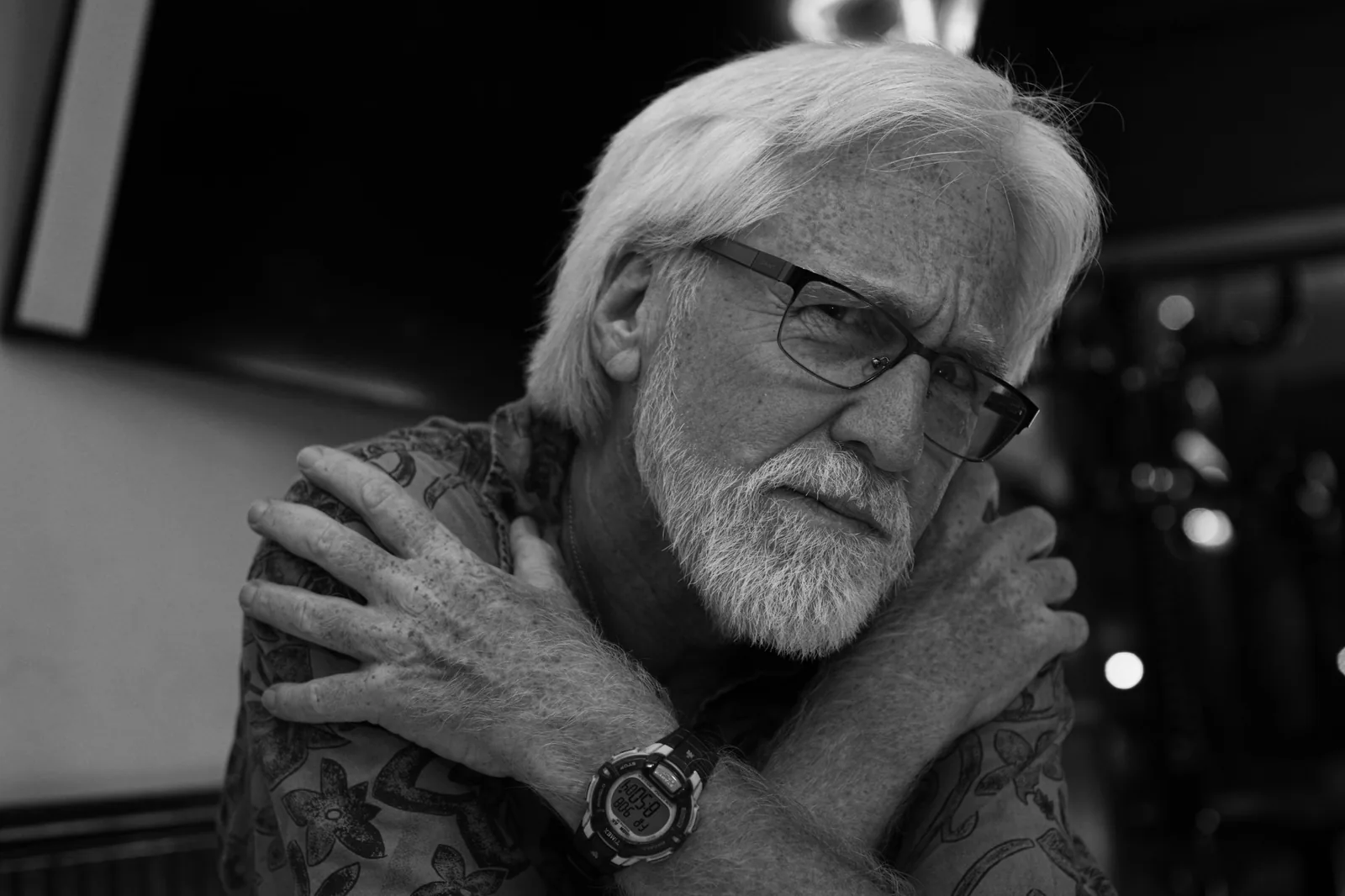 Black and white portrait of a man with white hair and glasses, arms crossed