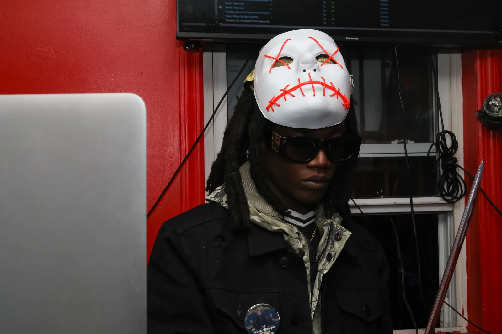 DJ in a white stitched mask performing behind a laptop