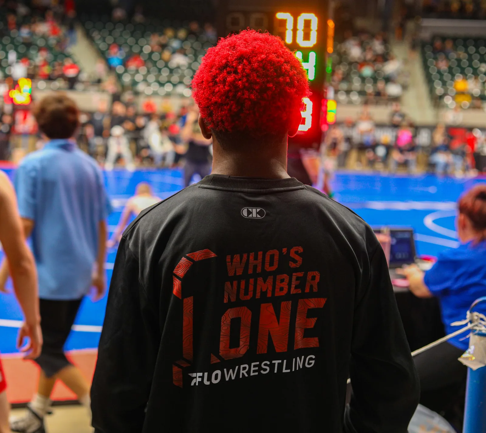 Wrestler with red hair watching the mat under the scoreboard at a tournament